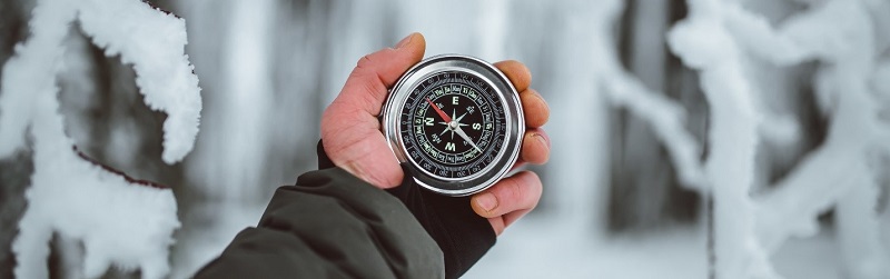 using a compass in a snowy forest an adventurer checks their direction